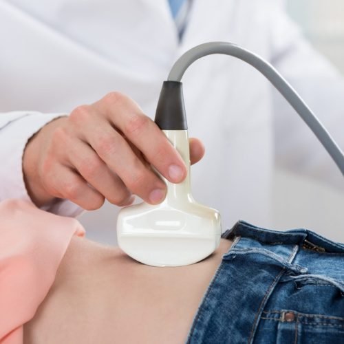 Closeup of male doctor moving ultrasound probe on pregnant woman's stomach in hospital